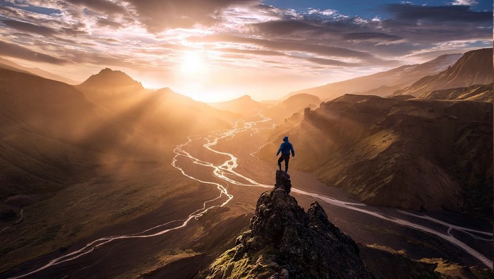 Man on cliff overlooking river valley at sunset