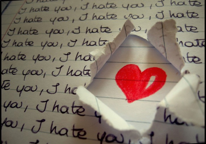 Torn paper revealing a red heart drawn on a notebook page with "I hate you" written repeatedly.