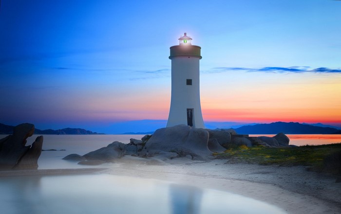 Lighthouse on rocky shore at sunset