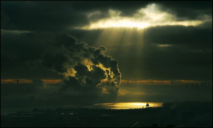 Smoke from industrial chimneys over a river at sunset