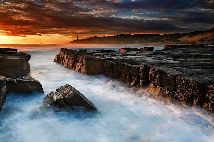 Sunset over rocky coast with lighthouse