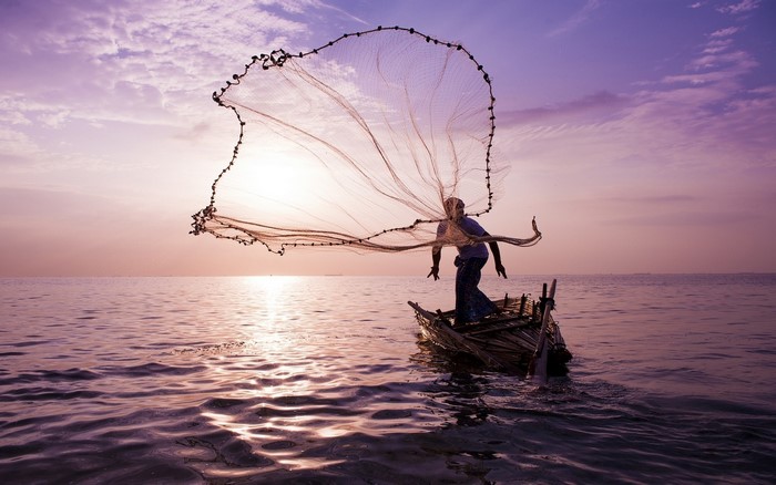 Fisherman casting net from boat at sunrise