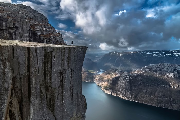 Man standing on cliff edge overlooking fjord in Norway