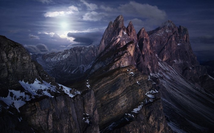 Dramatic mountain range under a cloudy sky with moonlight