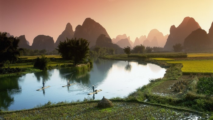 Men on rafts in a river with karst mountains and rice fields