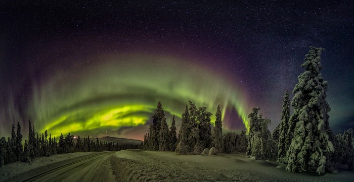 Aurora Borealis over snowy forest and road in Finland
