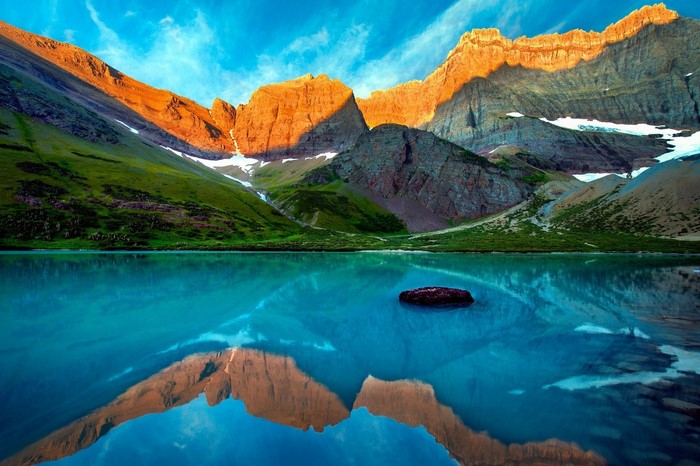 Turquoise lake reflecting mountains at sunset in Glacier National Park