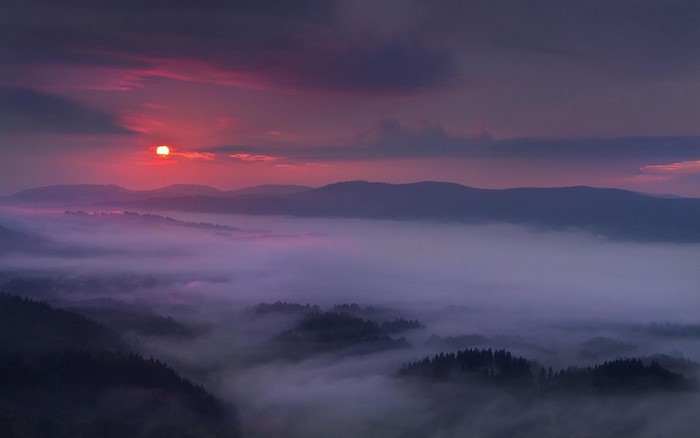Purple misty mountains at sunset with sun and clouds
