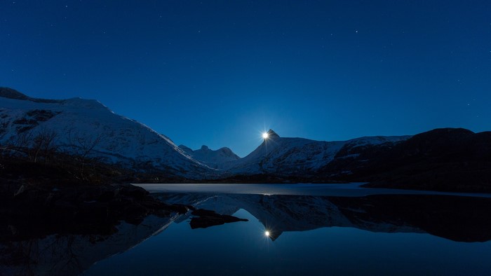 Moonlit snowy mountains reflected in a lake in Norway