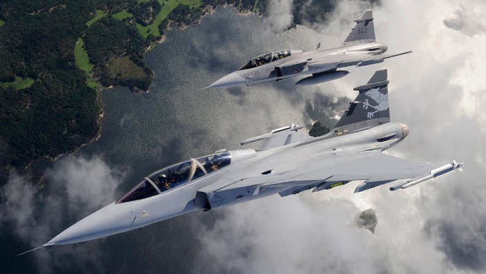 Two Swedish Air Force JAS 39 Gripen fighter jets flying over water and land