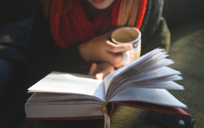 Woman reading a book and drinking from a mug