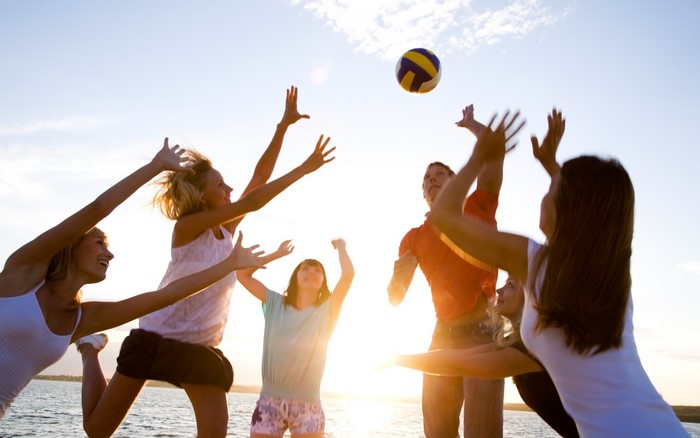People playing volleyball on a beach at sunset