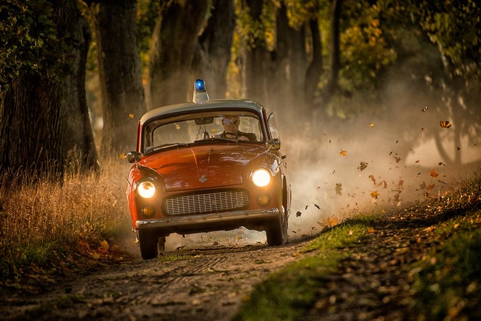 Orange Trabant car with blue light driving on dirt road