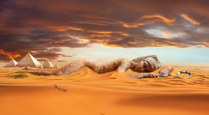 Giant Egyptian statue sleeping in desert with pyramids