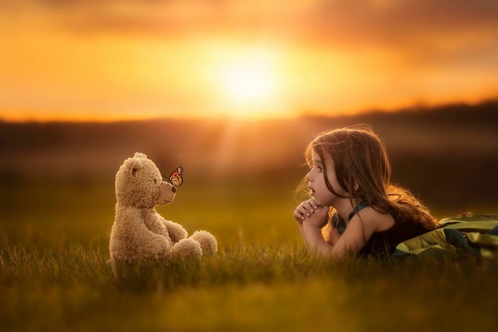 Girl and teddy bear with butterfly at sunset