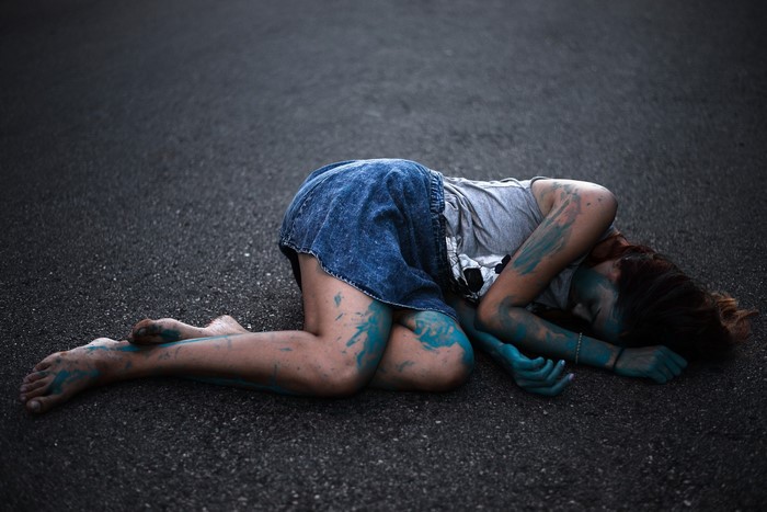 Woman with blue body paint lying on asphalt