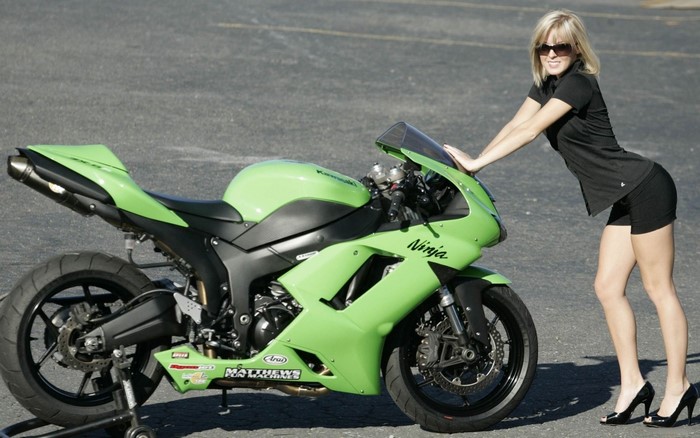 Woman in shorts and heels leaning on a green Kawasaki Ninja motorcycle