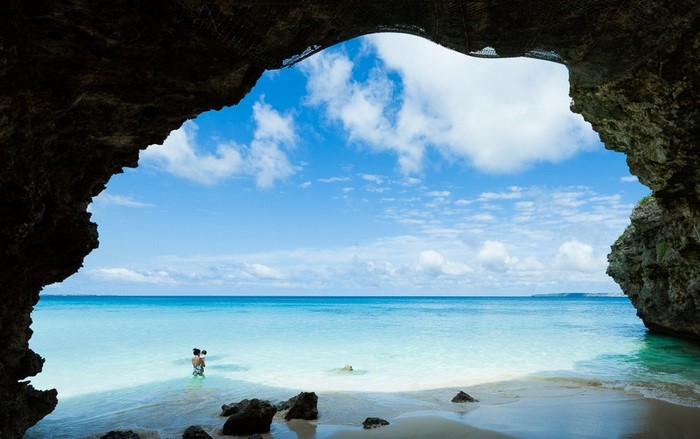 Couple with baby in a cave overlooking a tropical beach