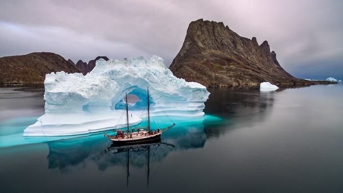 Sailing ship passes through an iceberg arch in Greenland