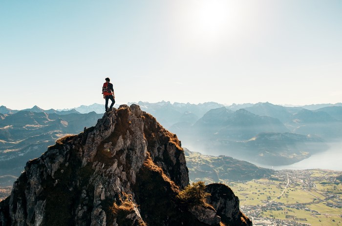 Man on mountain peak overlooking valley and lake