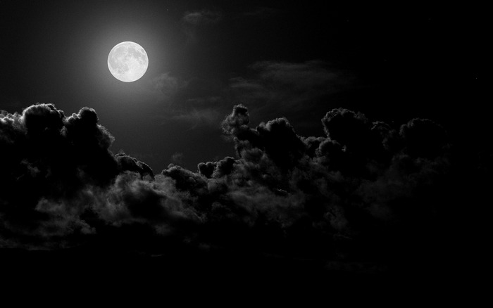 Full moon shining through dark clouds at night