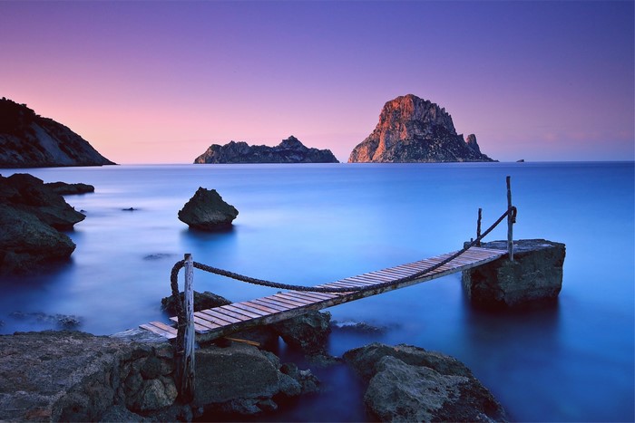 Wooden pier and rocky islands in the sea at sunset