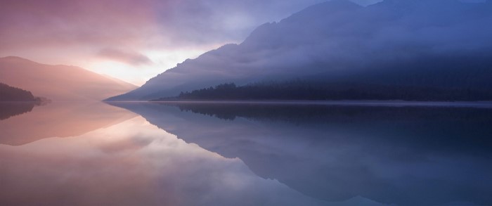 Misty mountains reflected in a calm lake at sunrise