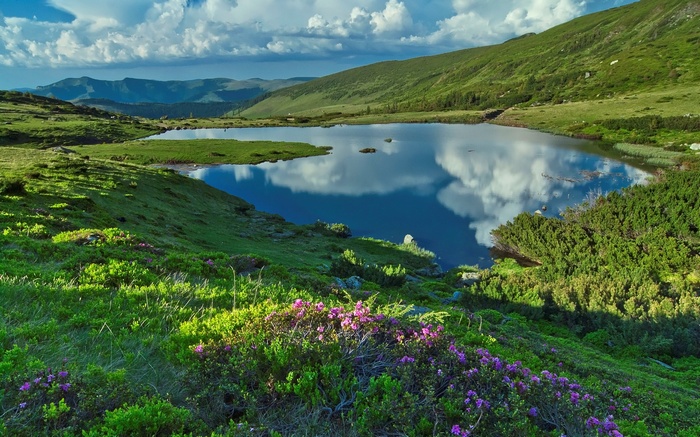 Mountain lake reflecting clouds and sky with green hills