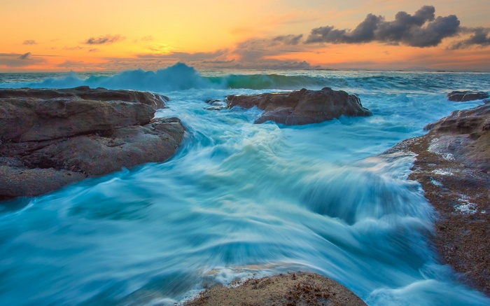 Ocean waves crashing on rocks at sunset