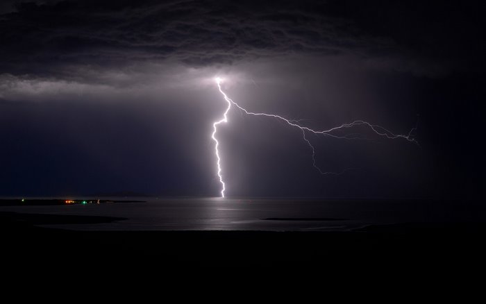 Lightning strikes the ocean during a dark storm