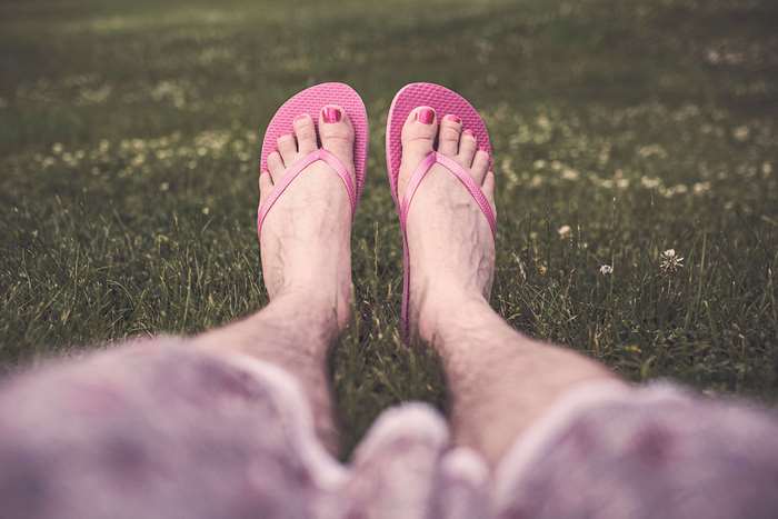 Man with pink toenails and flip flops relaxing on grass