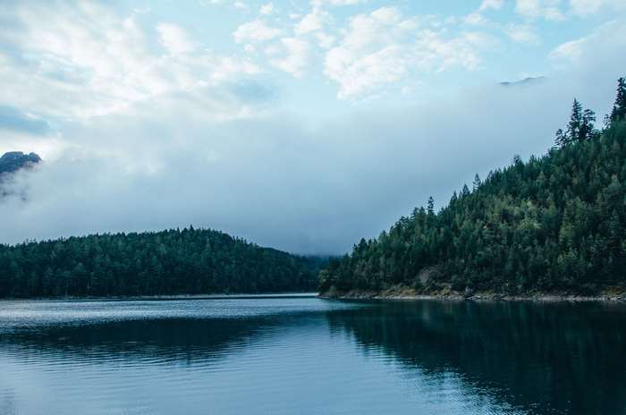 Lake surrounded by pine forest and clouds