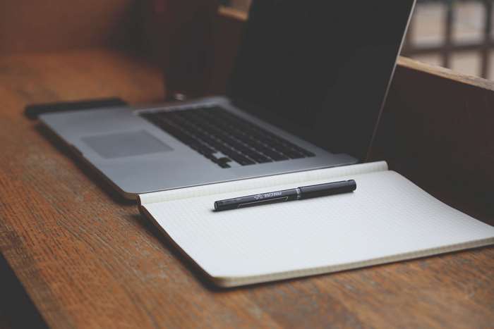 MacBook Pro with notebook and pen on wooden desk