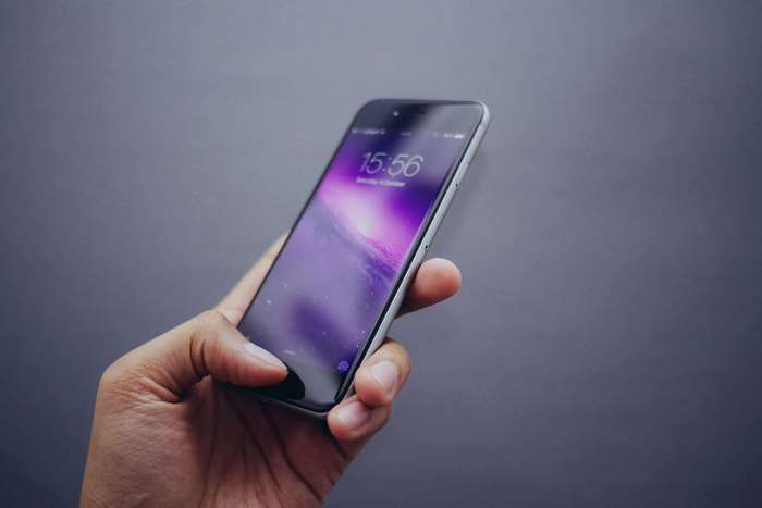 Hand holding iPhone 6 with lock screen showing time 15:56