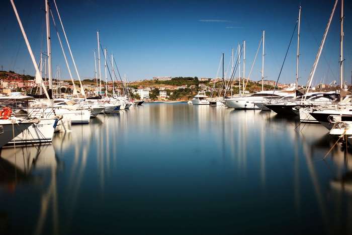 Sailboats and yachts docked in a marina with a town on the hill
