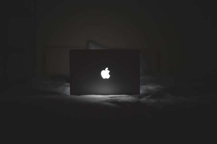 MacBook with glowing Apple logo on a bed in the dark 4K