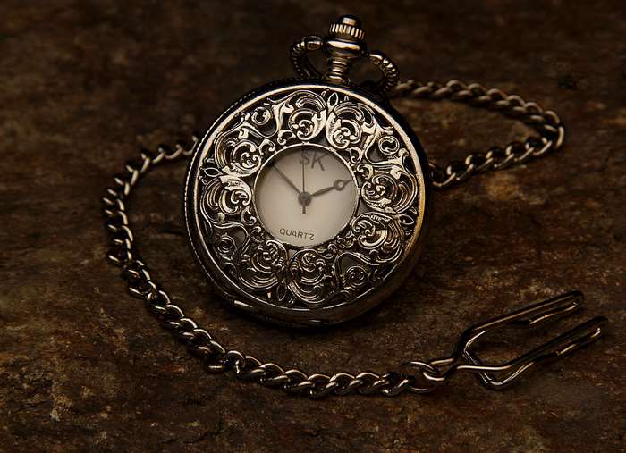 Ornate pocket watch with chain on stone surface
