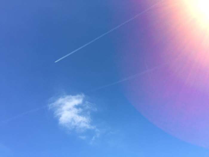 Airplane contrail in a bright blue sky with sun flare