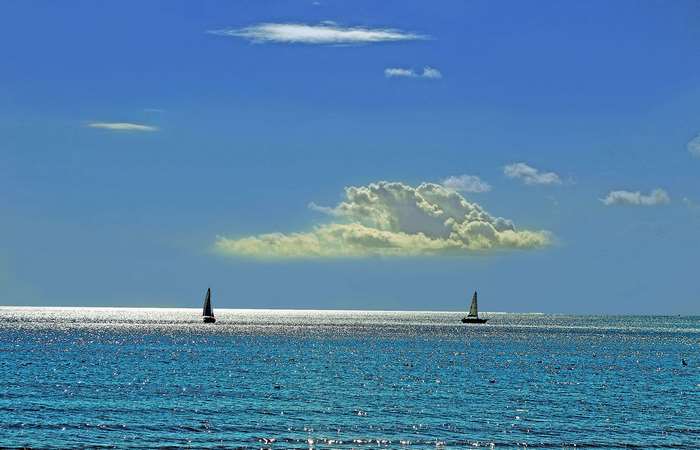 Sailboats on a bright blue ocean under a cloudy sky