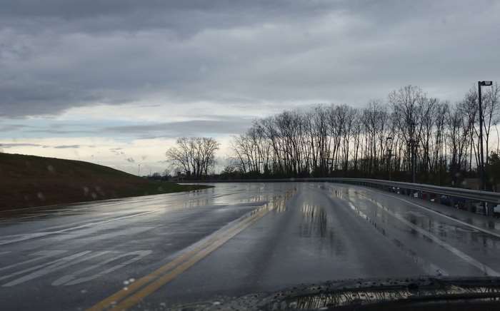 Wet road with trees and cloudy sky
