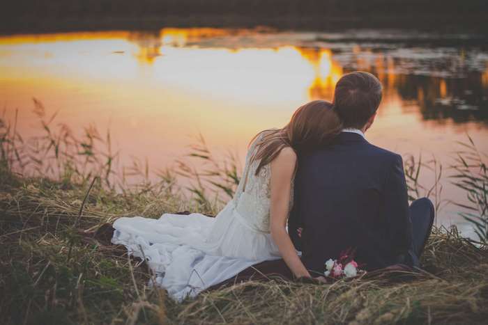 Bride and groom sitting by a lake at sunset