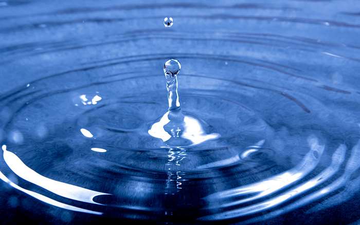 Water drop creating ripples in blue water 4K