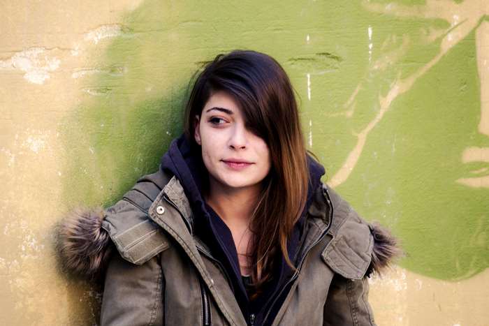 Young woman in a jacket leaning against a wall