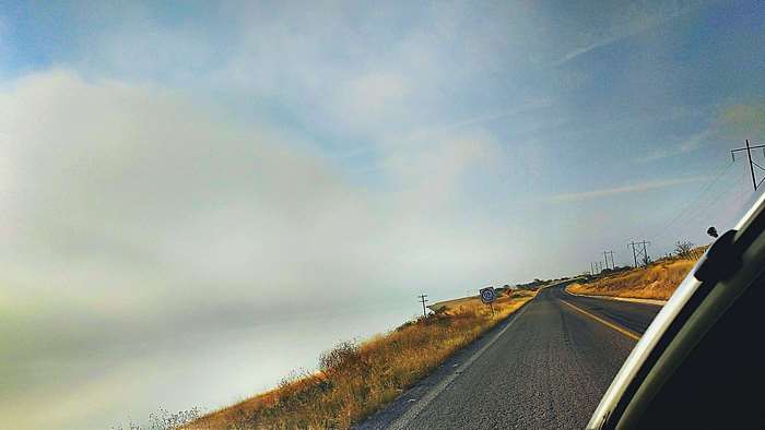 Road through a landscape with clouds and power lines