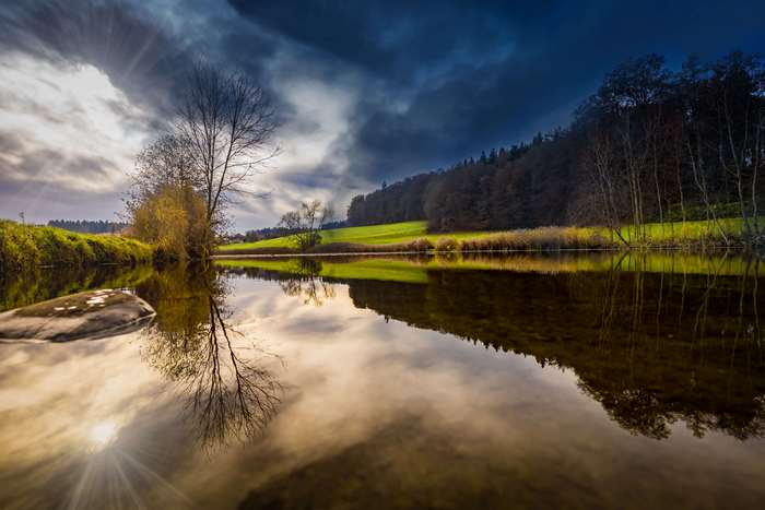River reflecting trees and dramatic clouds at sunset