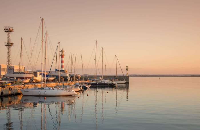 Sailboats docked in a harbor at sunset with lighthouse