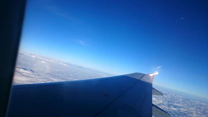 Airplane wing flying over clouds in blue sky