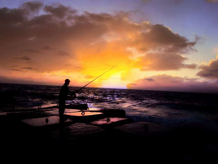 Man fishing on rocks at sunset