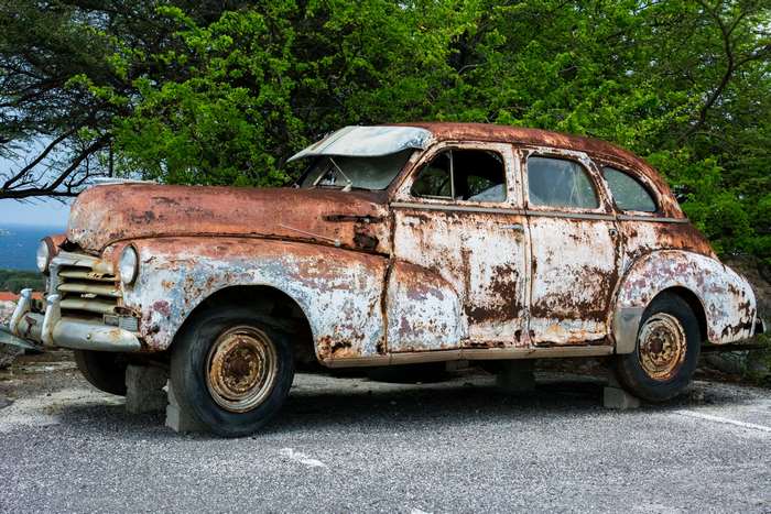 Rusted vintage car in front of green trees