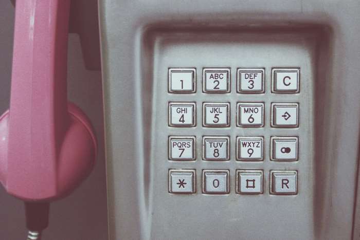 Close-up of a vintage payphone with a pink handset and keypad